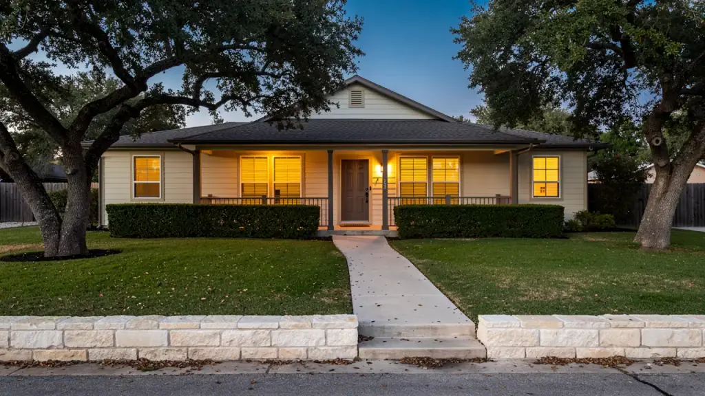 Central Texas home at dusk with warm light in the windows and a swept front walk